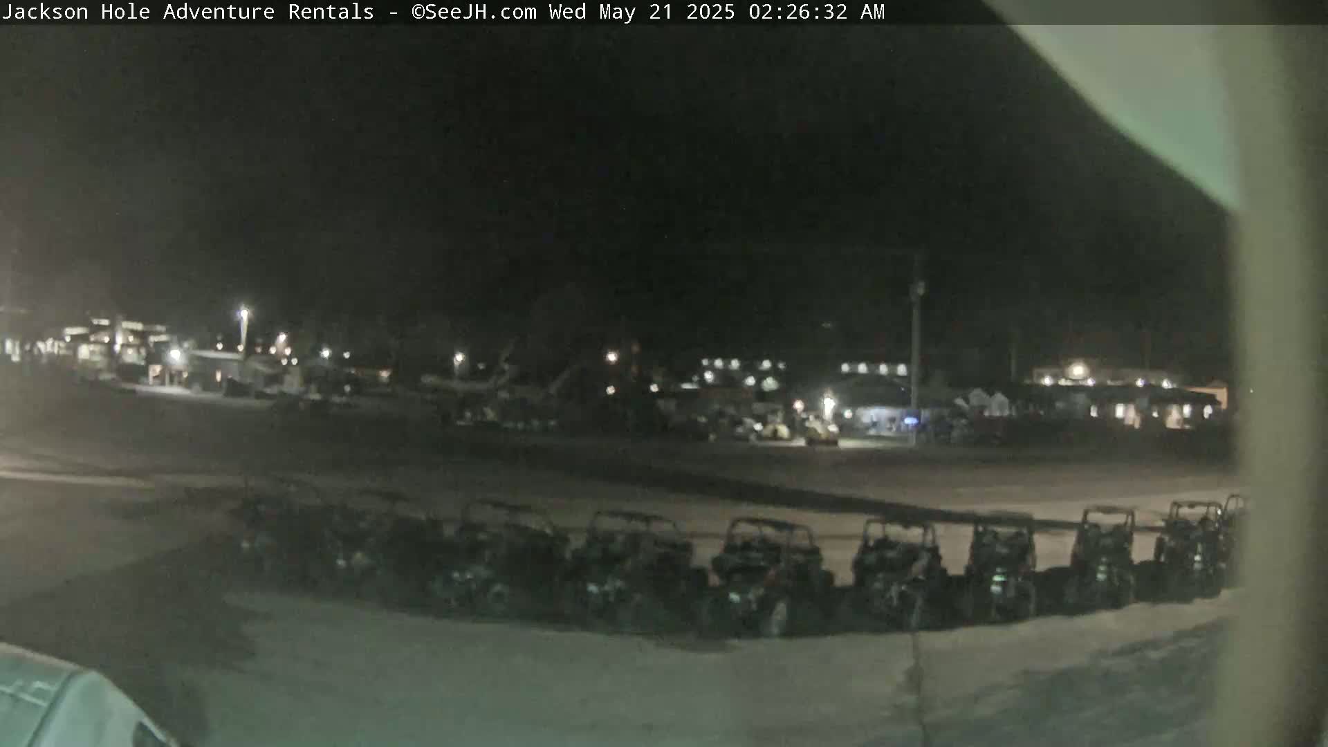A nighttime outdoor scene shows a row of parked all-terrain vehicles in a lot, with other vehicles and buildings visible in the background under dark, clear skies.