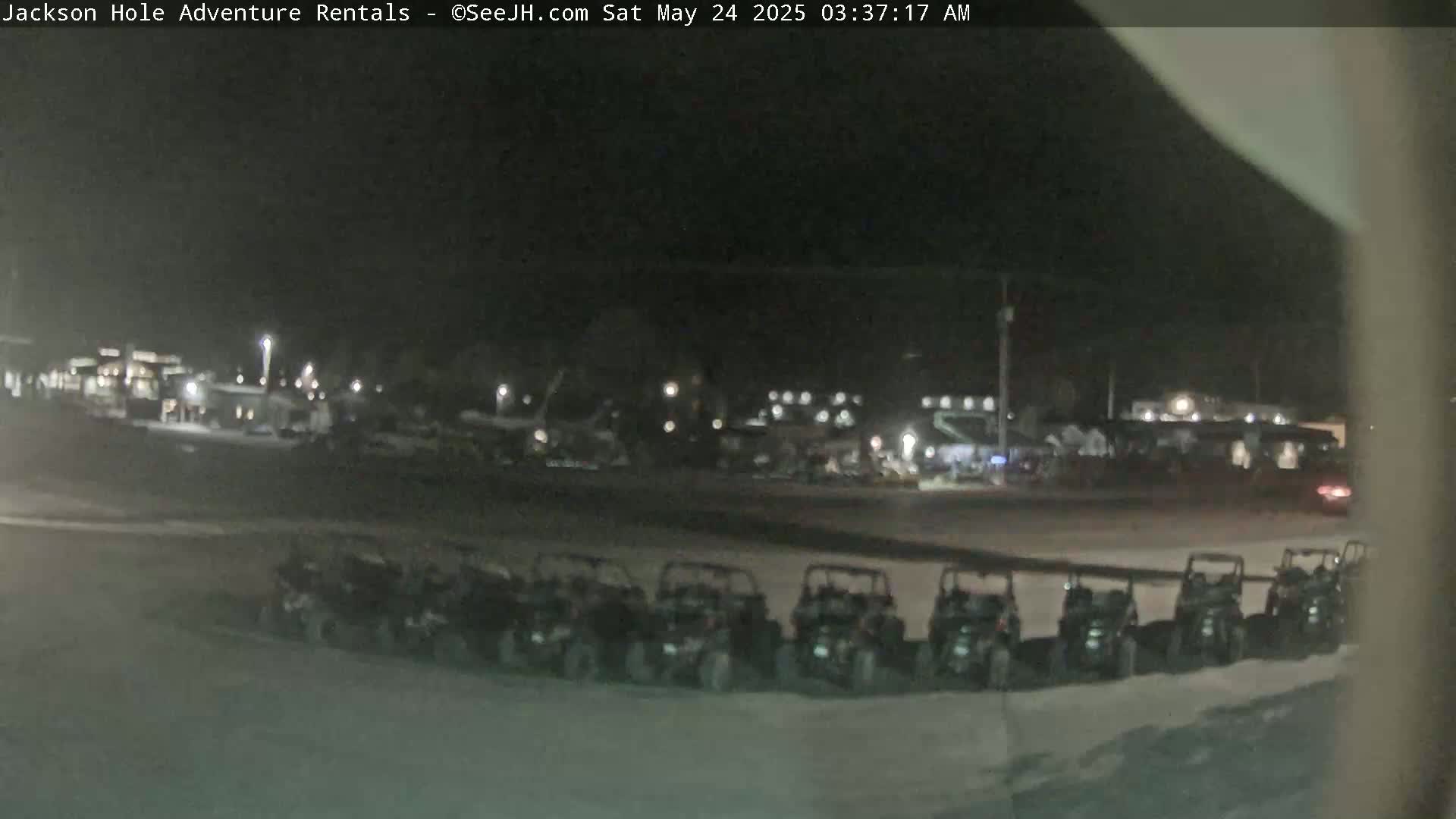 A nighttime, outdoor scene shows a row of parked all-terrain vehicles in front of a building complex.