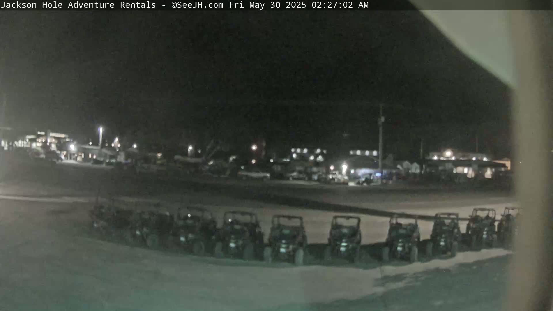 A nighttime, snowy scene shows a row of parked all-terrain vehicles in front of a building.
