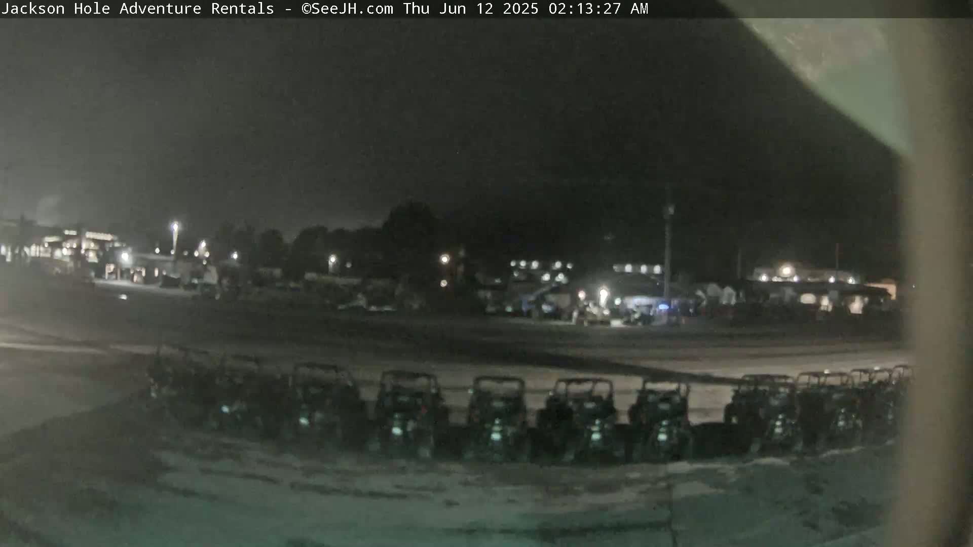 At night, a row of all-terrain vehicles is parked in a lot near a dimly lit building.