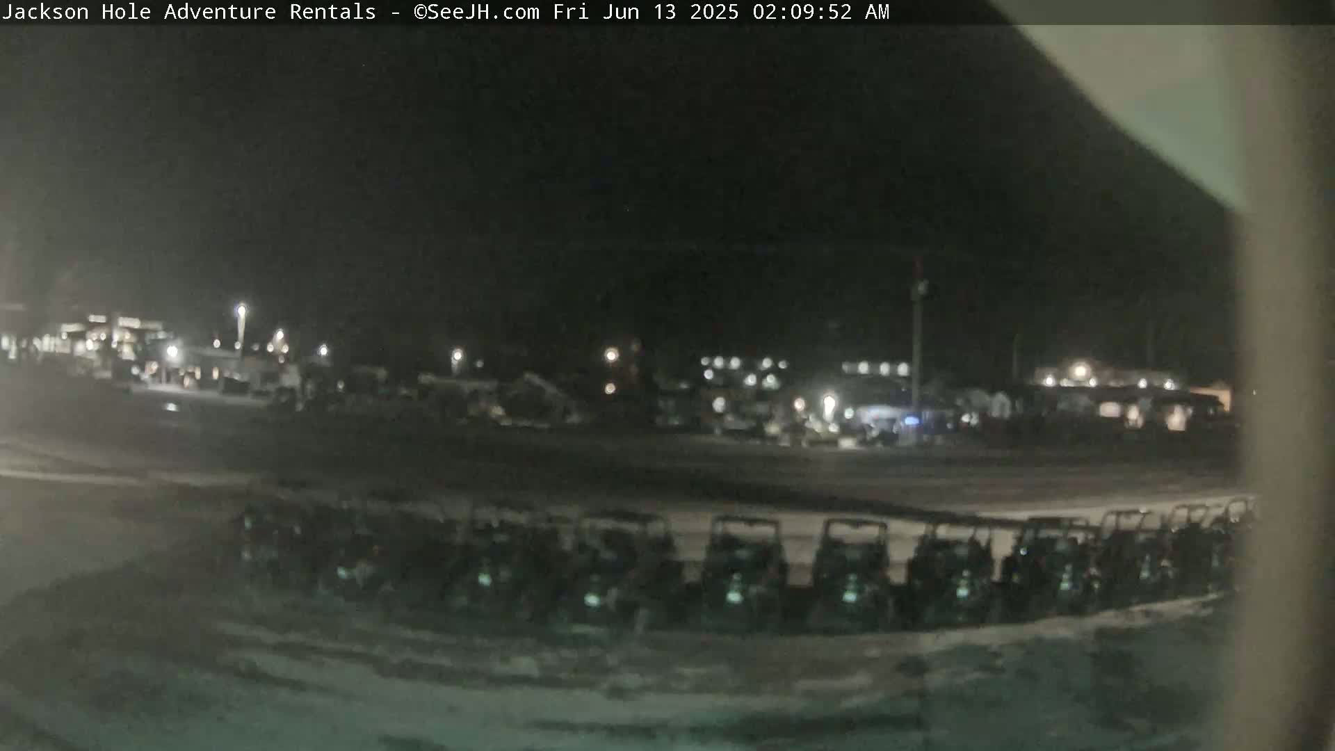 A nighttime, snow-covered parking lot contains a row of parked all-terrain vehicles in front of a dimly lit building.