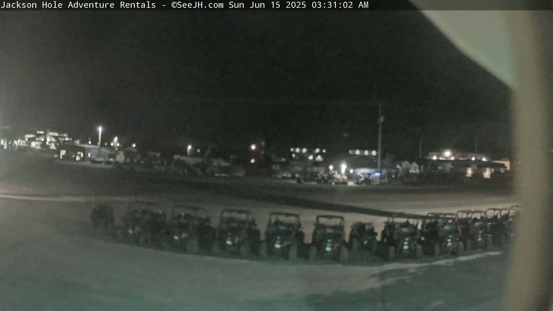 A nighttime, outdoor scene shows a row of parked off-road vehicles in a parking lot near a building, under dark skies.