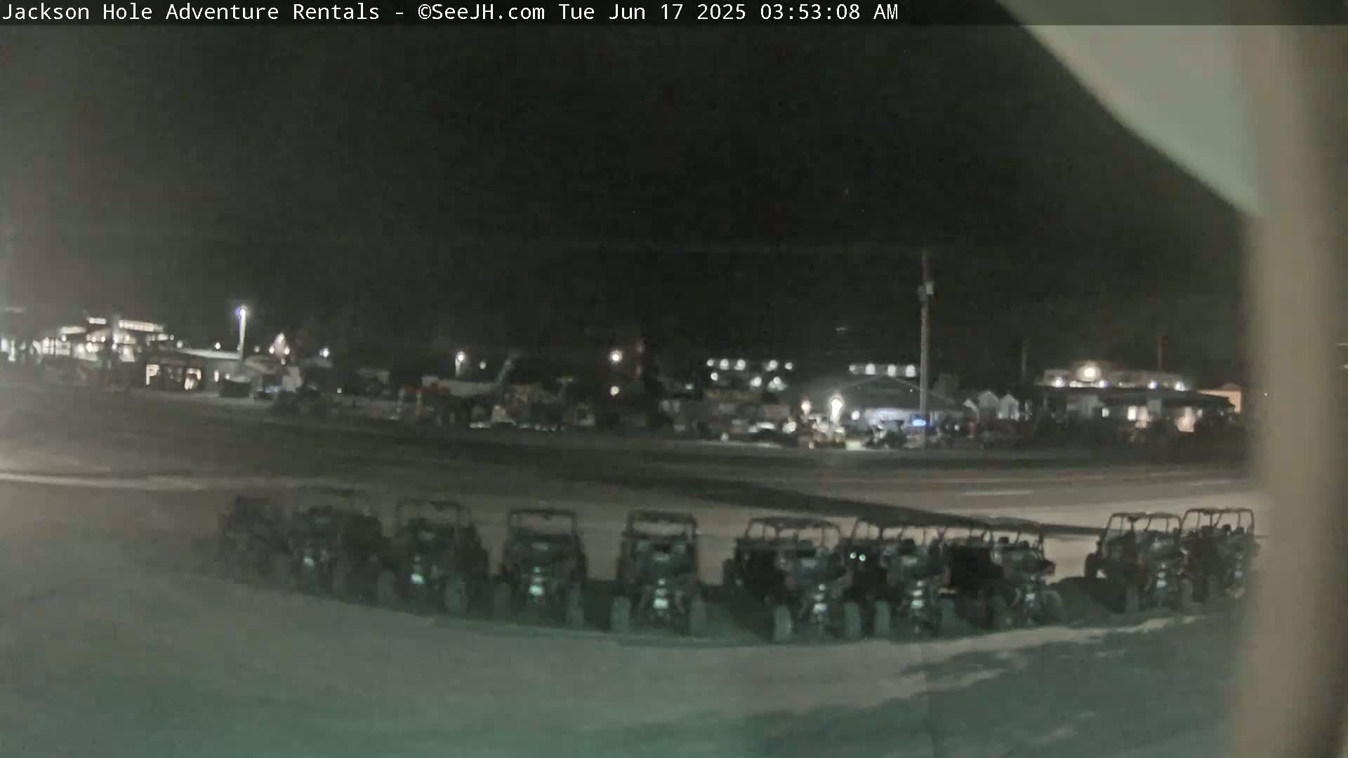 At night, a row of parked all-terrain vehicles sits in a parking lot in front of a building, under dark, clear skies.