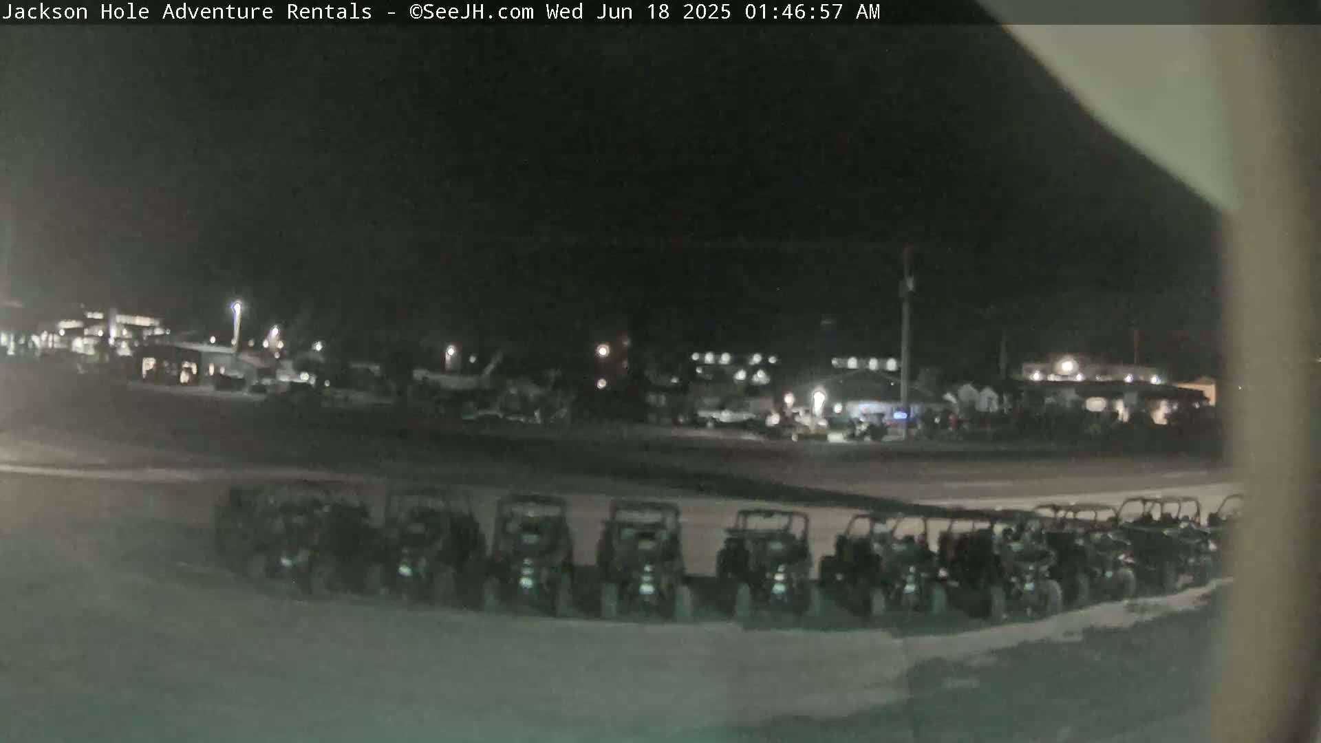 A row of all-terrain vehicles is parked in a lot at night under dark skies.