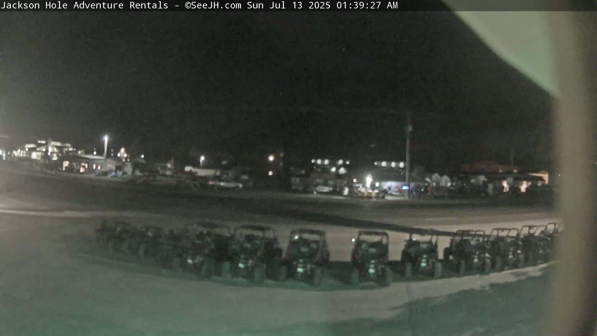 A nighttime, dimly lit parking lot contains a row of parked off-road vehicles in front of a building.