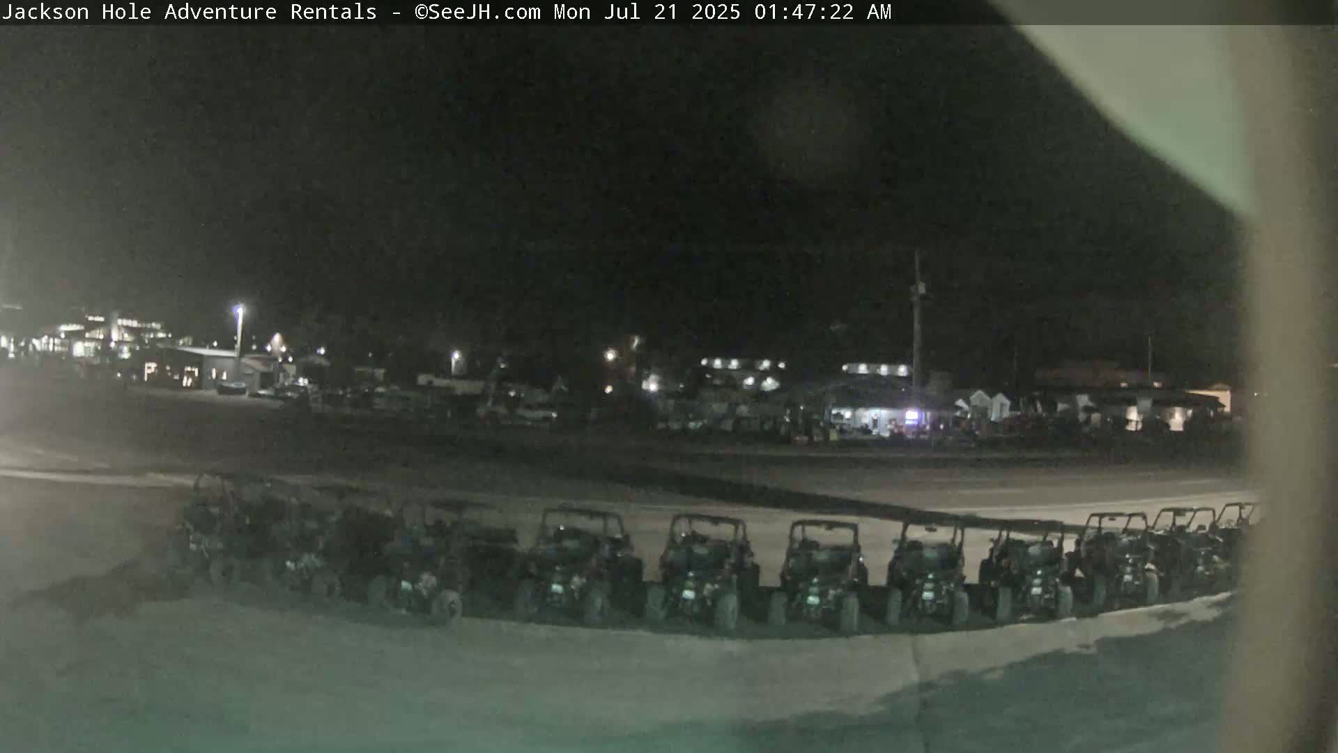 A row of parked all-terrain vehicles is visible at night, in front of a dimly lit building and parking lot.
