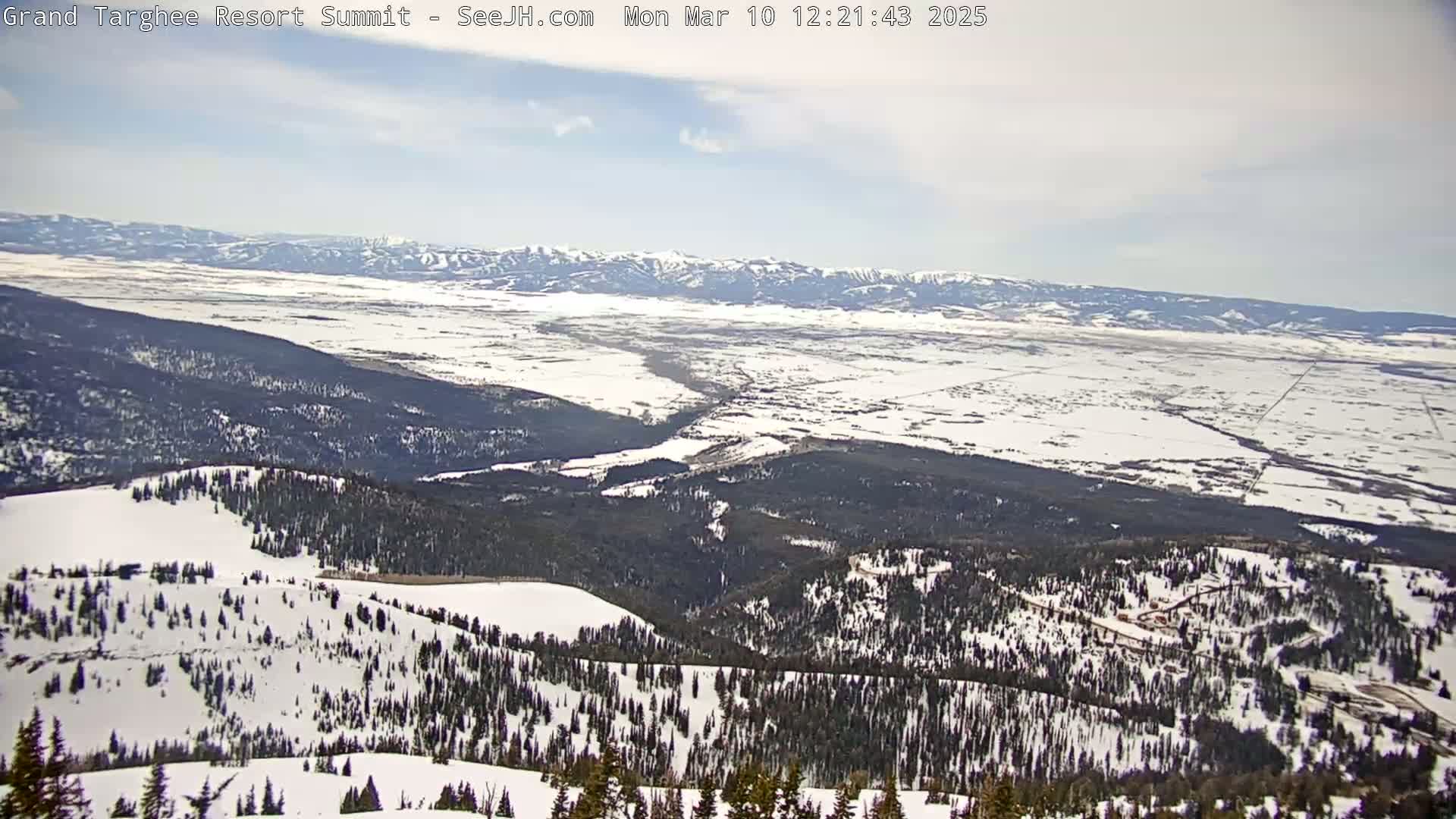 A snow-covered mountain range and valley extend to distant, snow-capped mountains under a mostly clear sky.