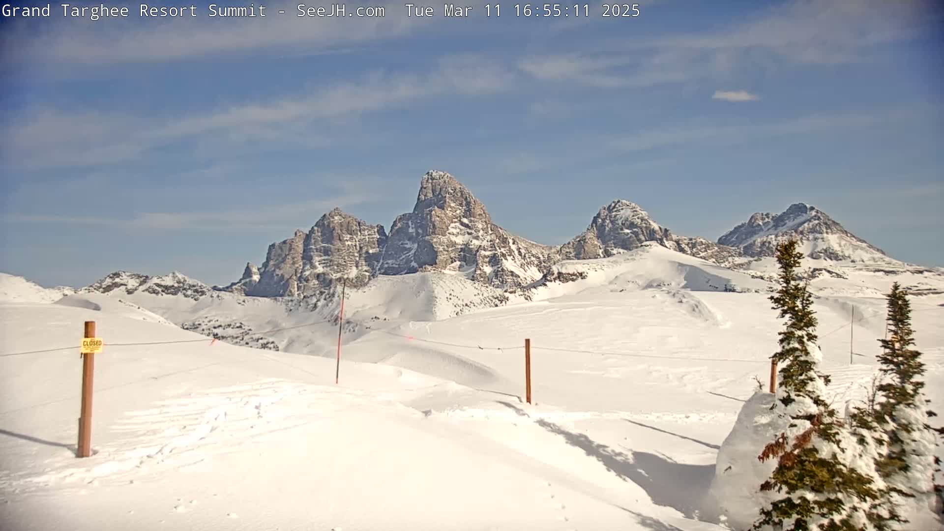 A snow-covered landscape with several snow-capped mountain peaks under a mostly clear, sunny sky.