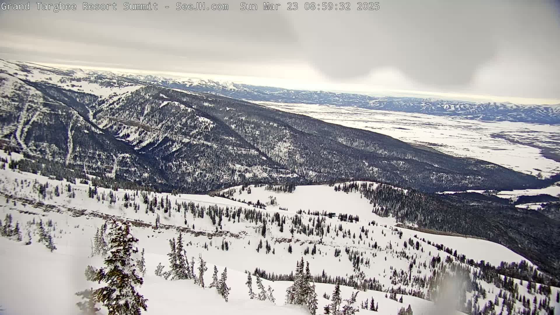 A snow-covered mountain range stretches to a valley under an overcast sky.