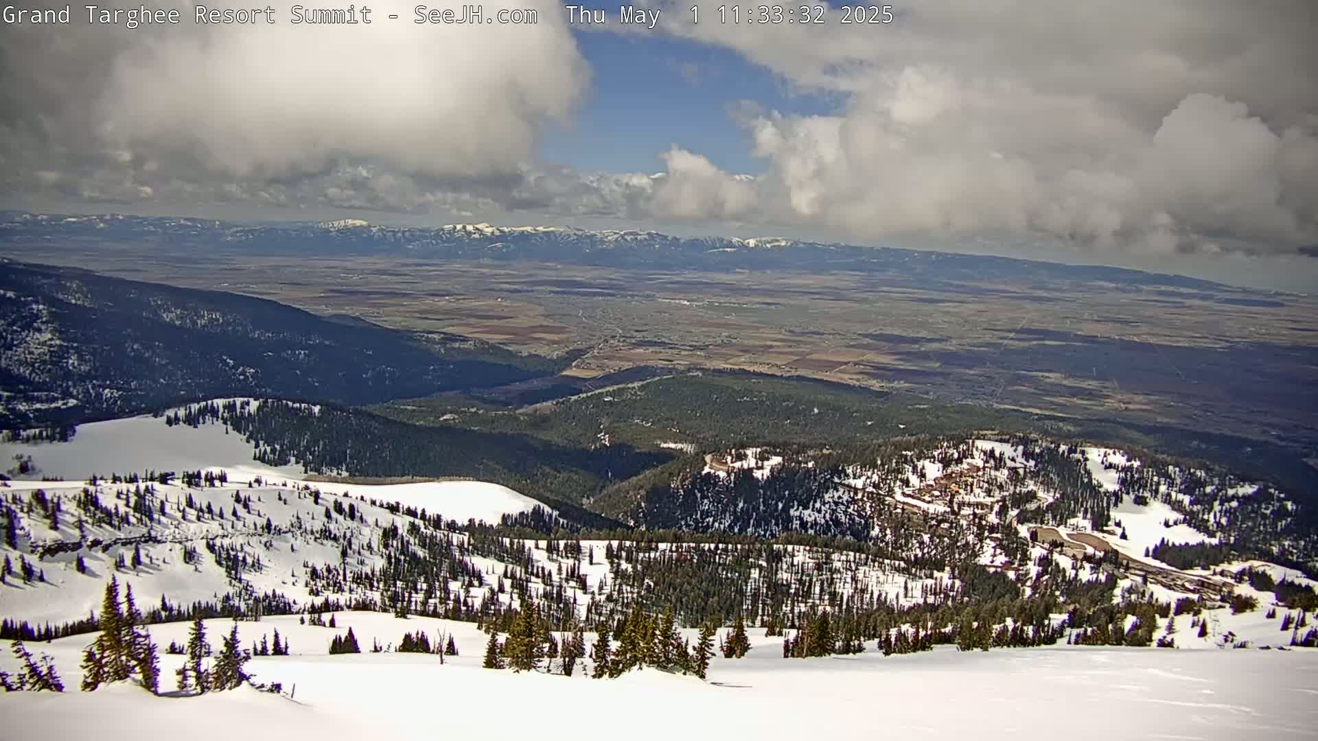 A snow-covered mountain vista reveals a vast valley under a partly cloudy sky.