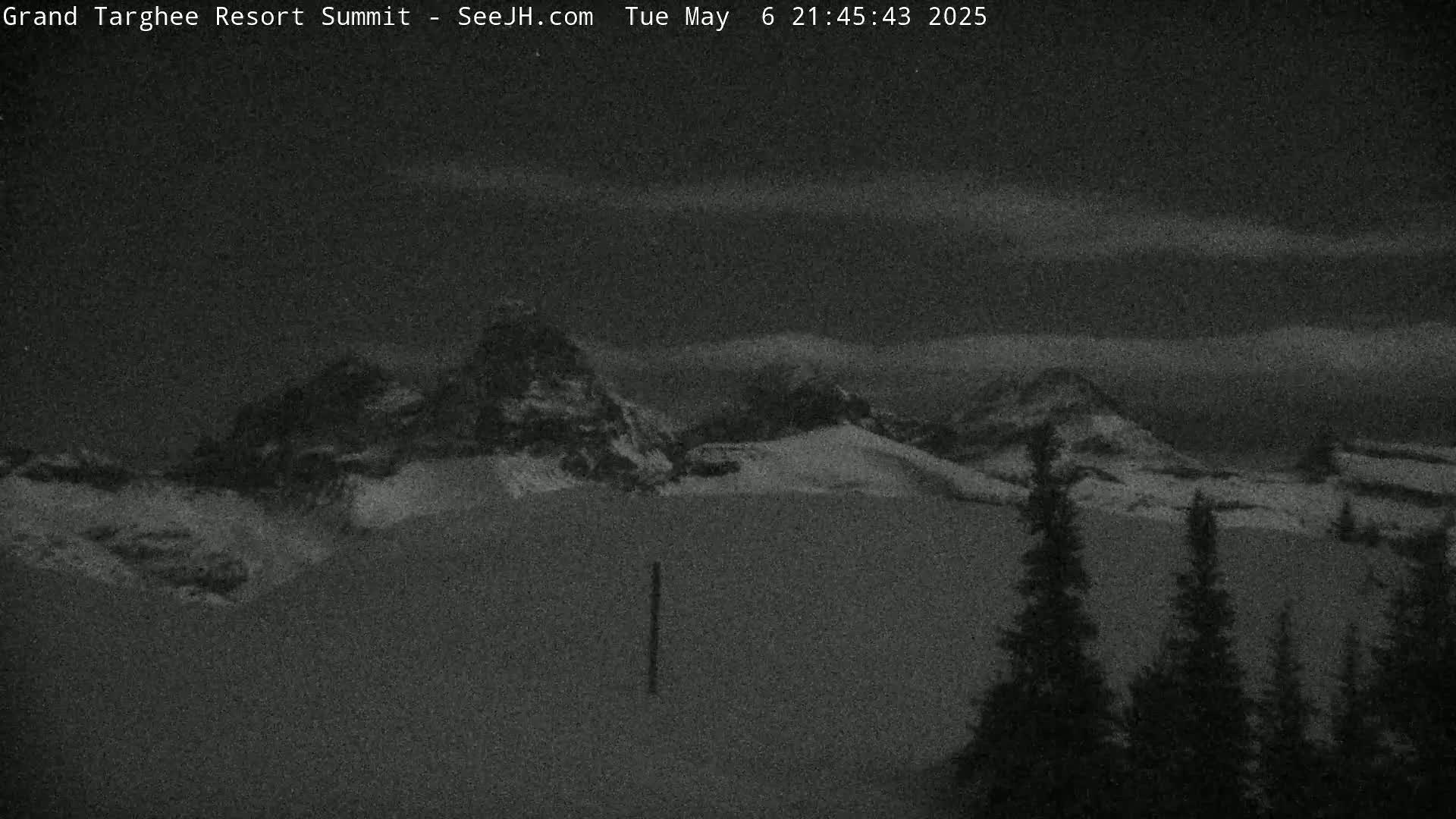 A nighttime view of snow-covered mountains under a partly cloudy sky.