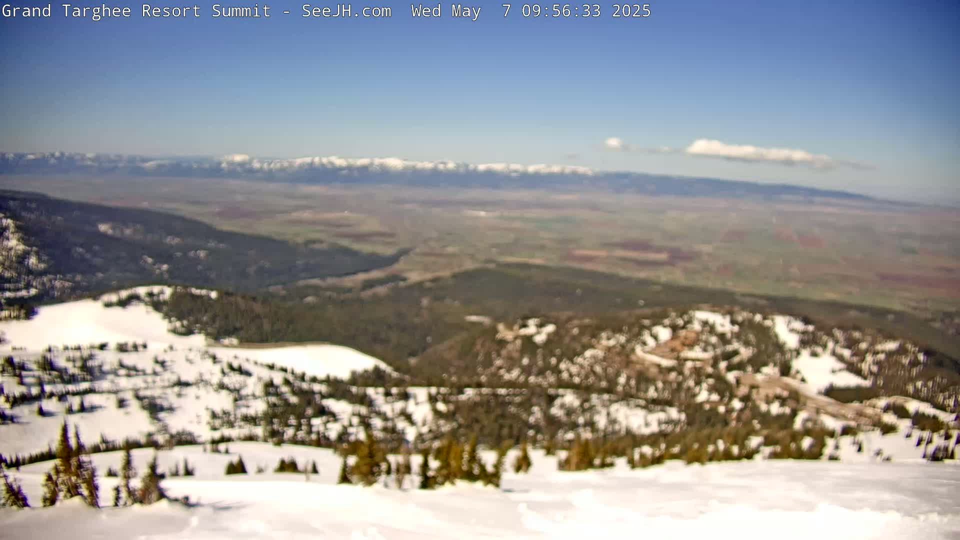 A snow-covered mountain peak overlooks a vast valley under a mostly clear blue sky with a single small cloud.