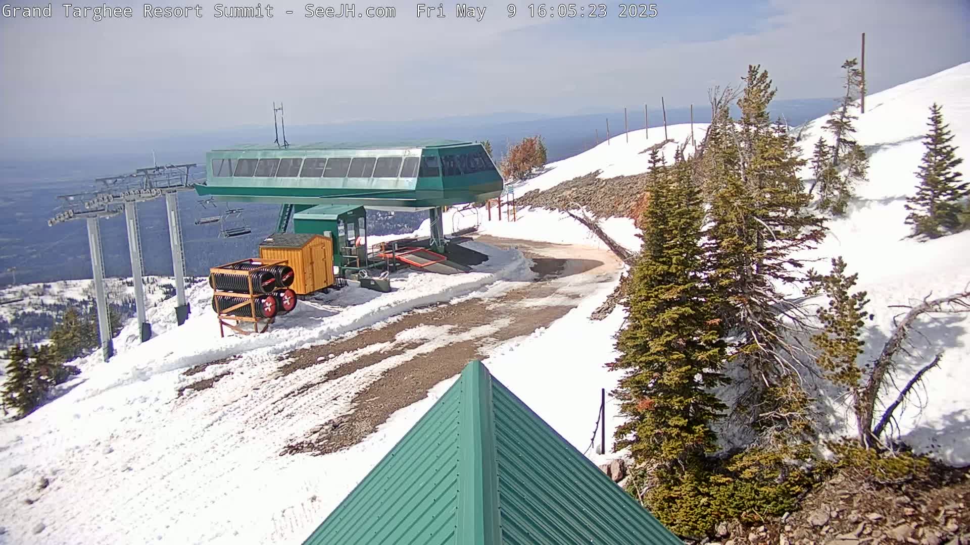 A ski lift station at a snowy mountaintop on a partly sunny day, with a dirt road leading away from it.