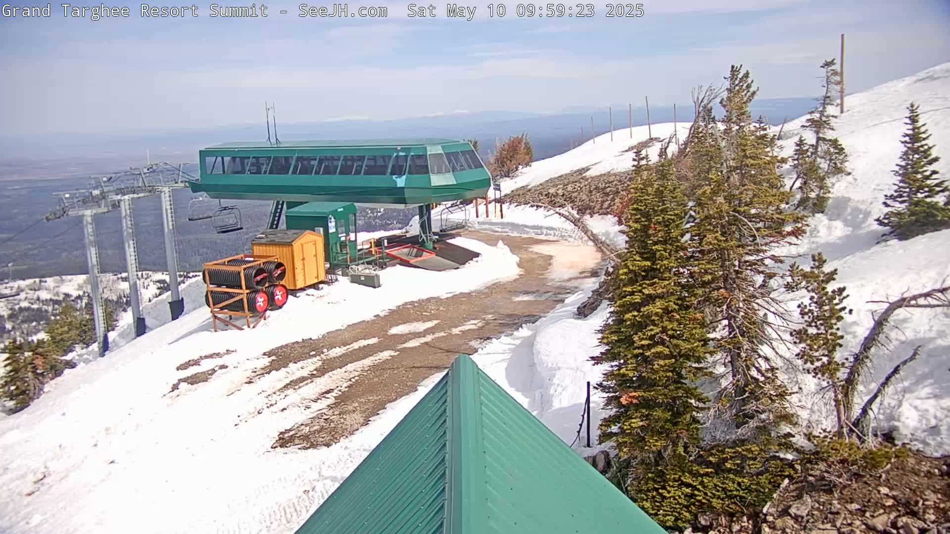 A green ski lift terminal sits atop a snow-covered mountain on a partly sunny day.