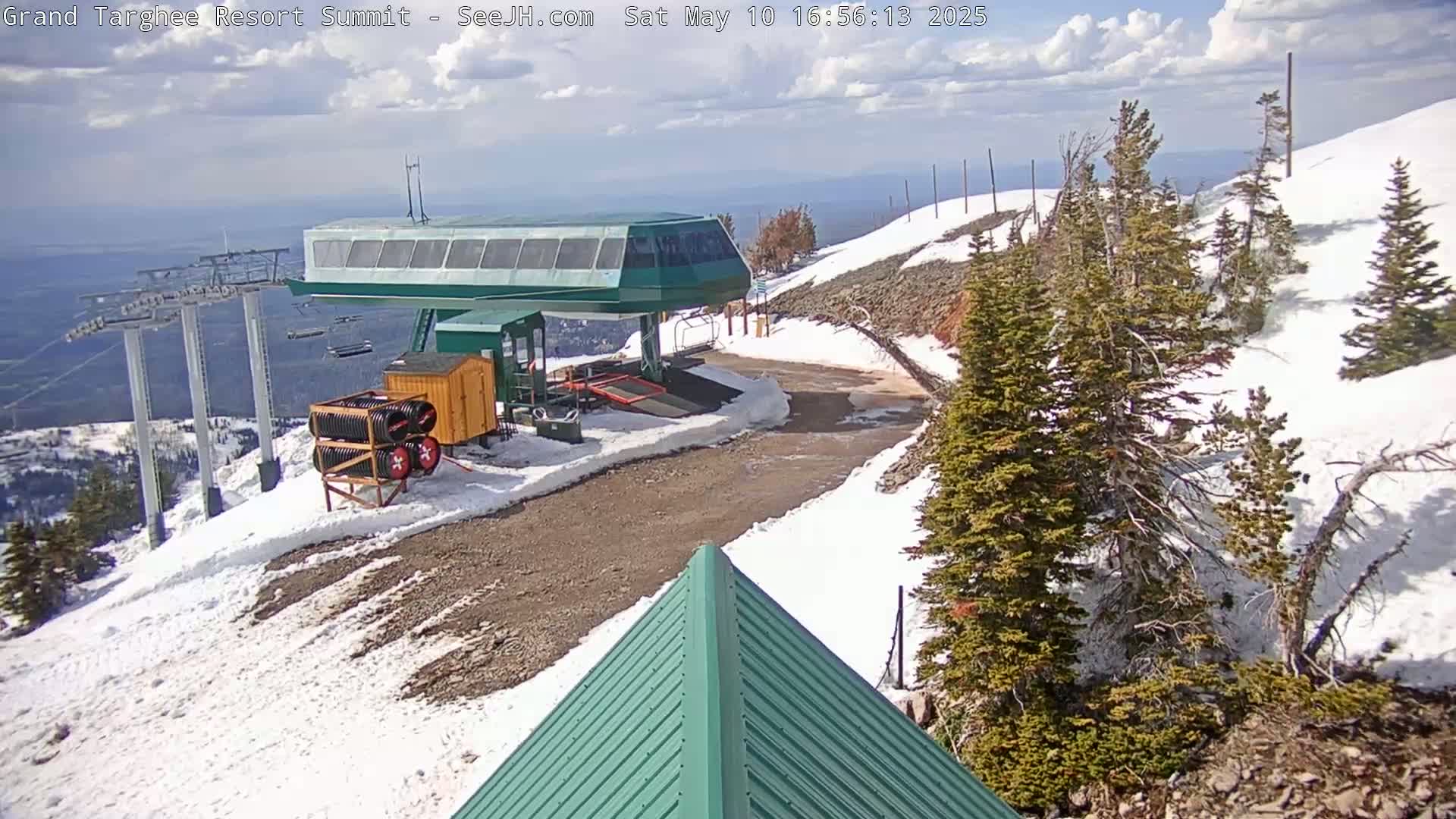 A ski lift station sits atop a snow-covered mountain on a partly cloudy day.