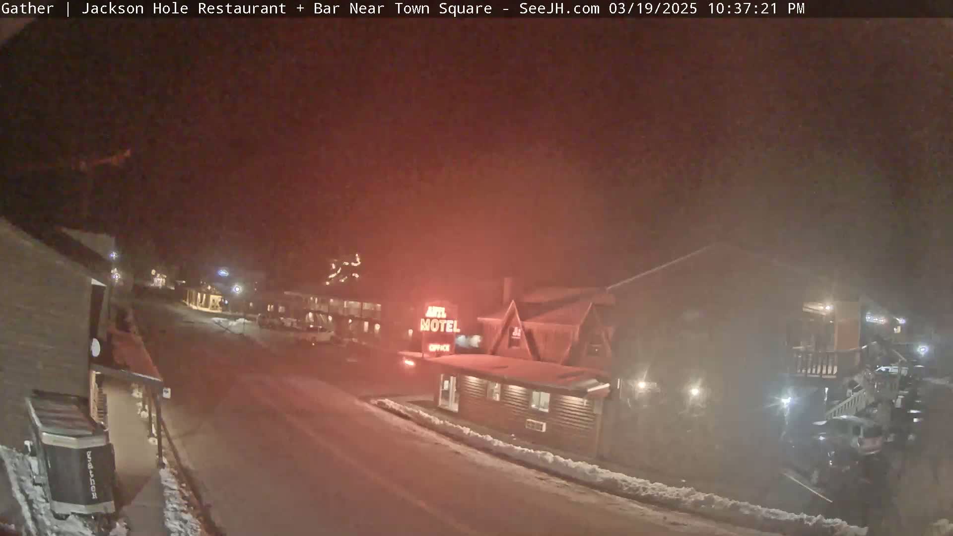 A nighttime, snowy street scene shows a motel and other buildings under a hazy, reddish sky.