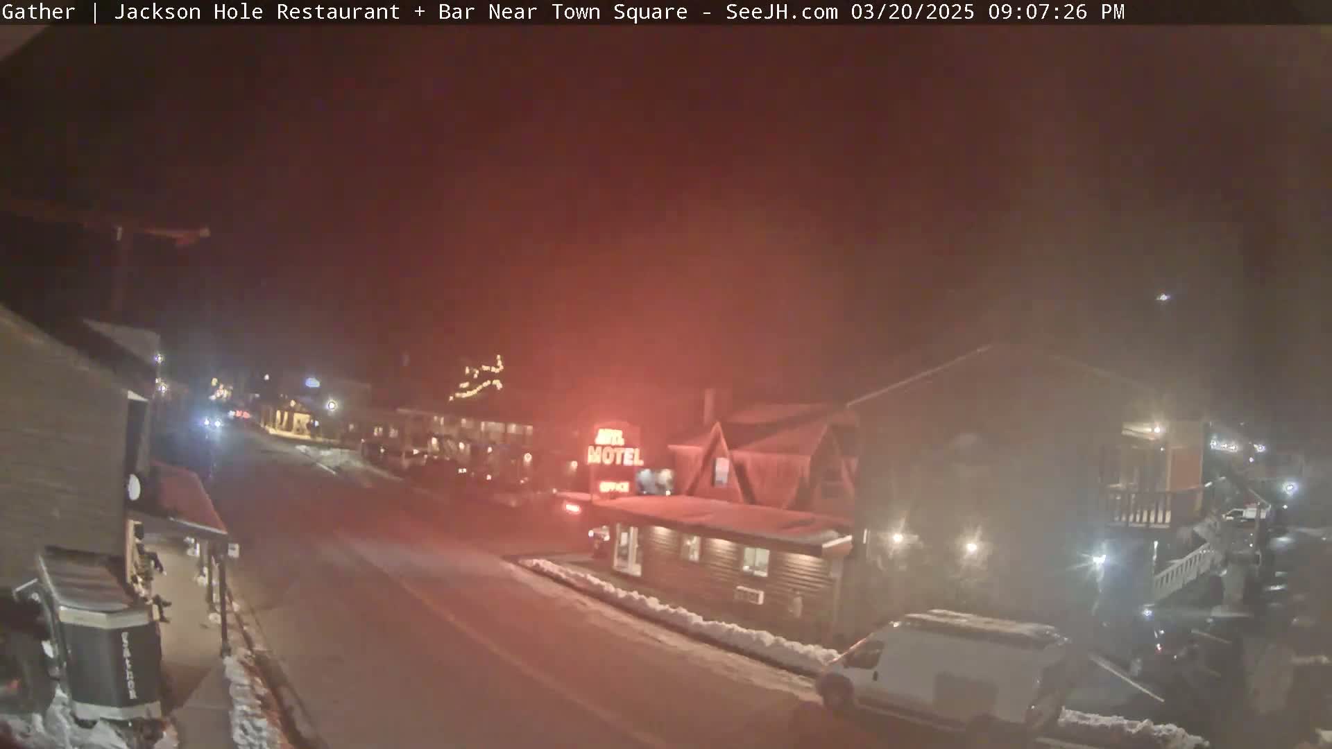 A nighttime street scene shows a motel and other buildings under a hazy, reddish sky with some snow on the ground.