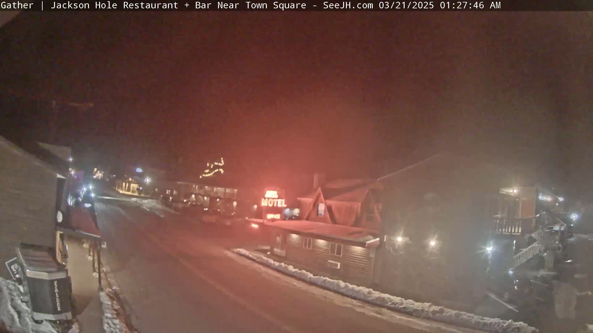 A nighttime street scene shows a motel and other buildings with some snow on the ground and a hazy atmosphere.