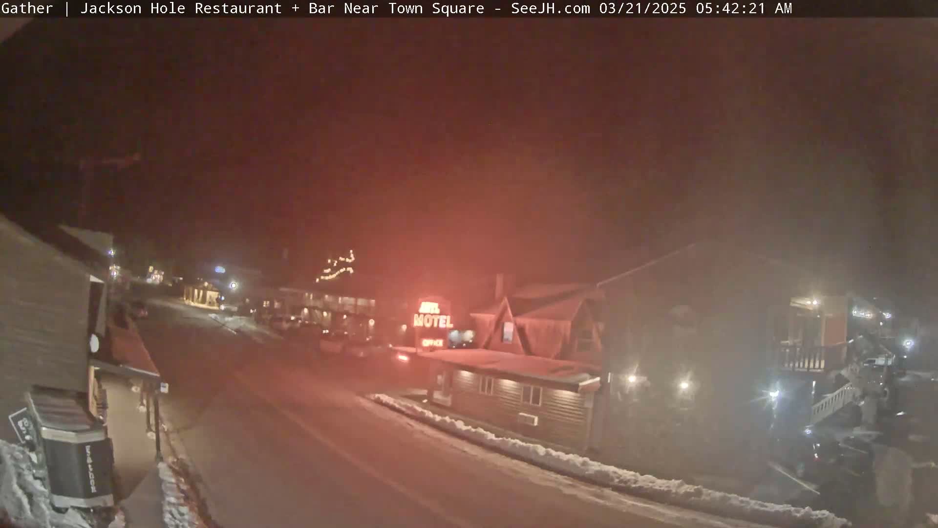 A nighttime street scene shows a motel and other buildings with some snow on the ground and a hazy atmosphere.