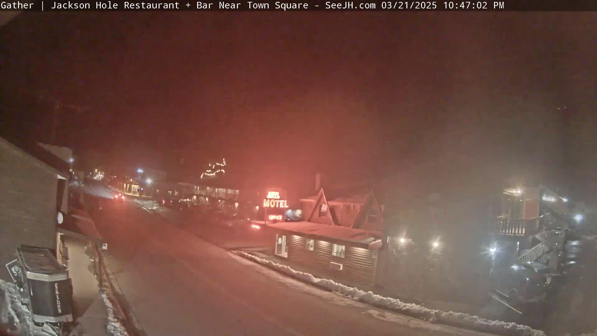 A nighttime street scene, lightly snowing, shows a motel and other buildings with some vehicle lights visible in the hazy distance.