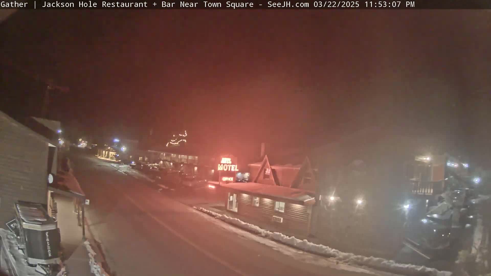 A nighttime street scene shows a motel and other buildings under a hazy, reddish sky with snow on the ground.