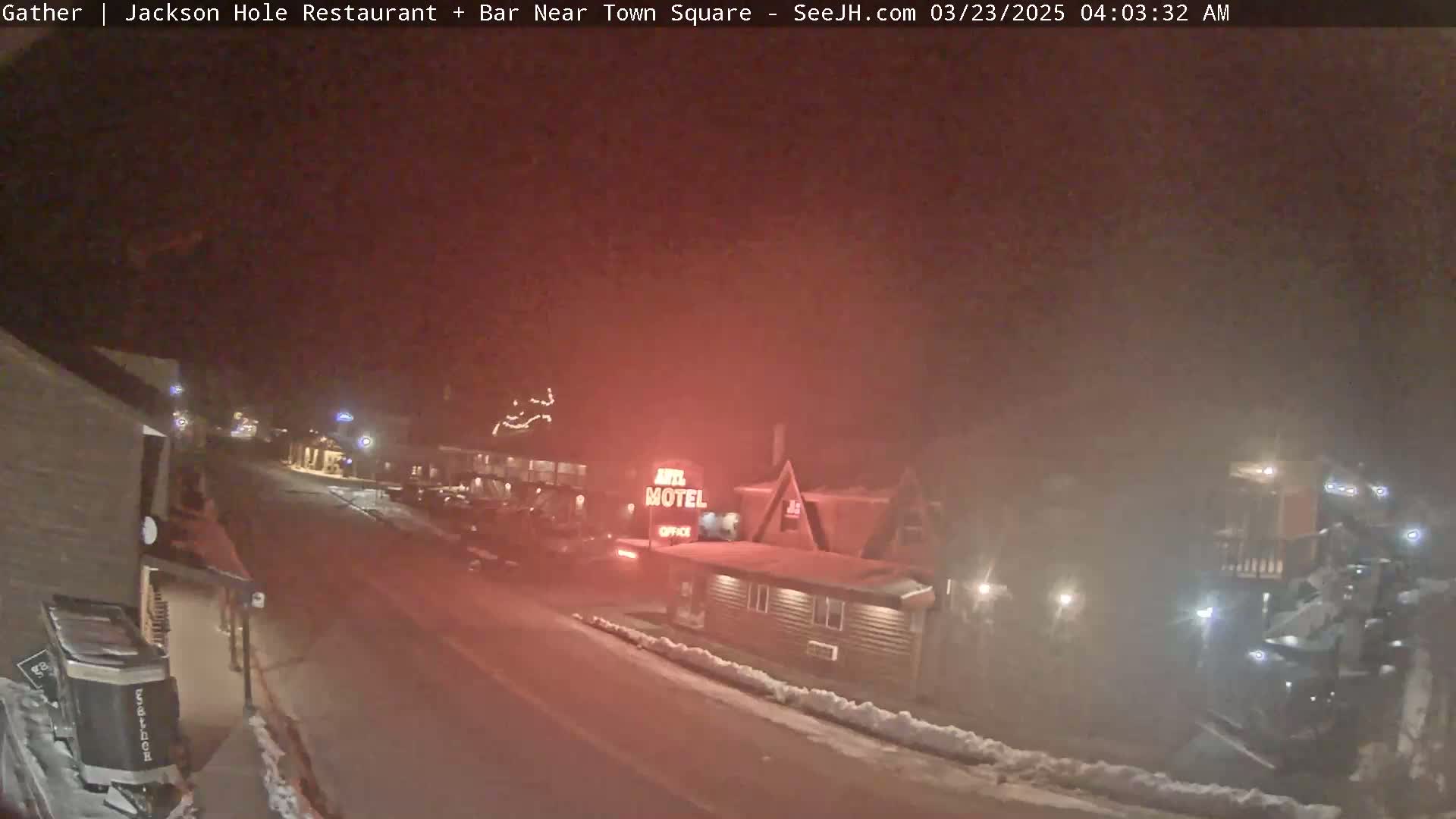 A nighttime, snowy street scene shows a motel and other buildings, with some vehicles visible in the hazy conditions.