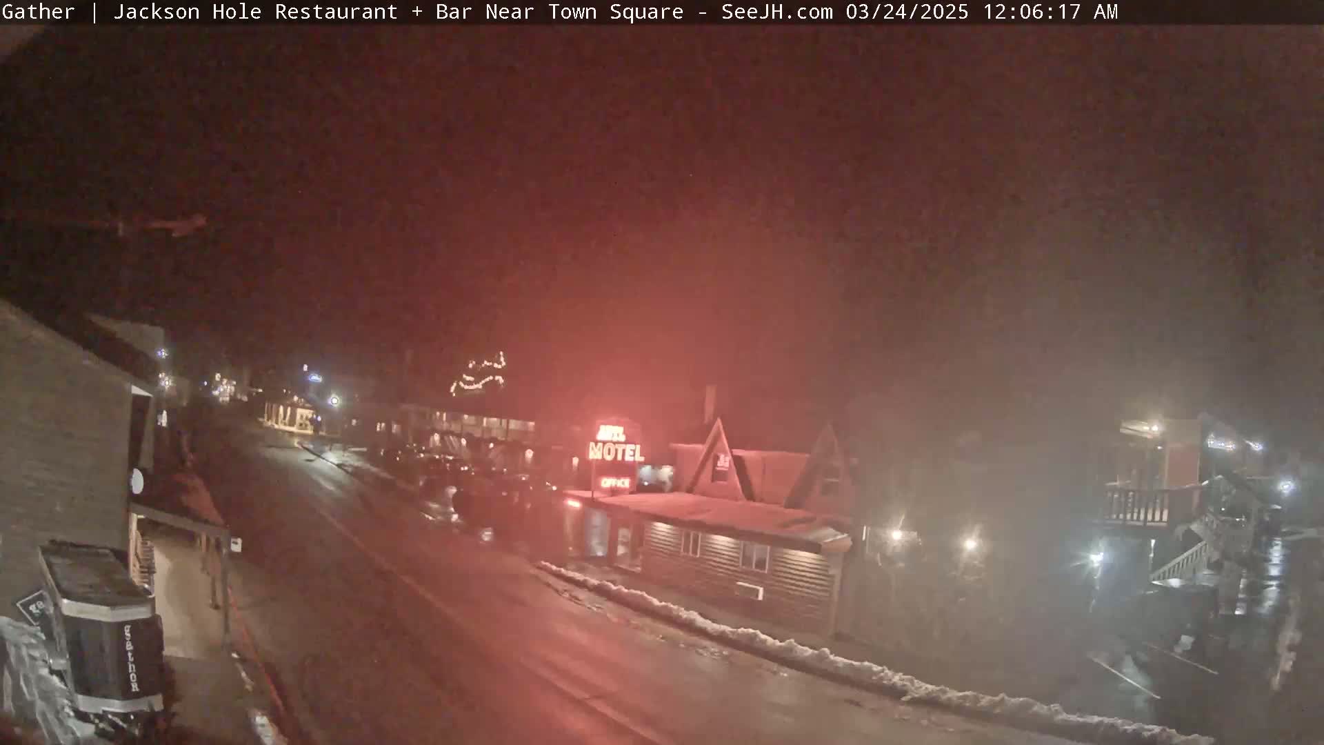 A nighttime street scene shows a motel and other buildings under a dark, hazy sky with some snow on the ground.