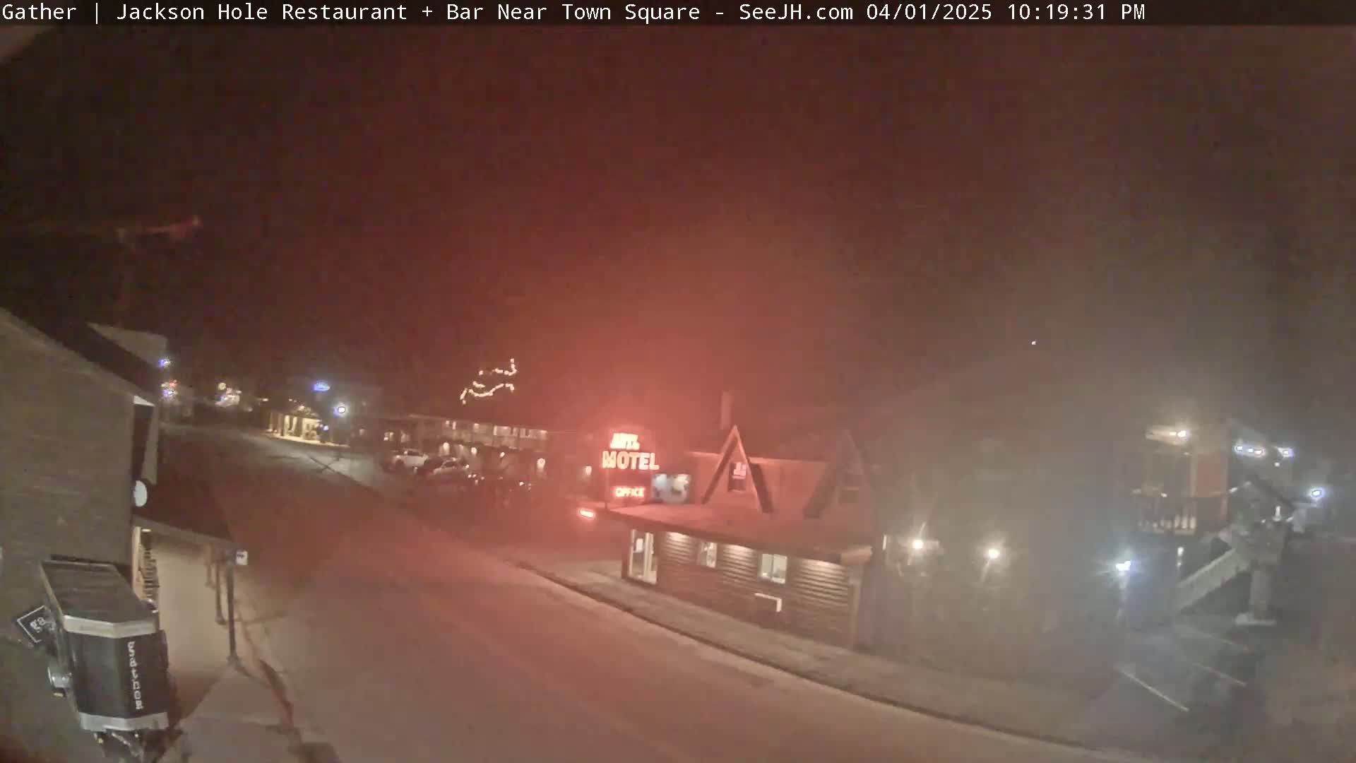 A nighttime street scene in hazy or foggy conditions shows a motel and other buildings, with some cars parked along the street.