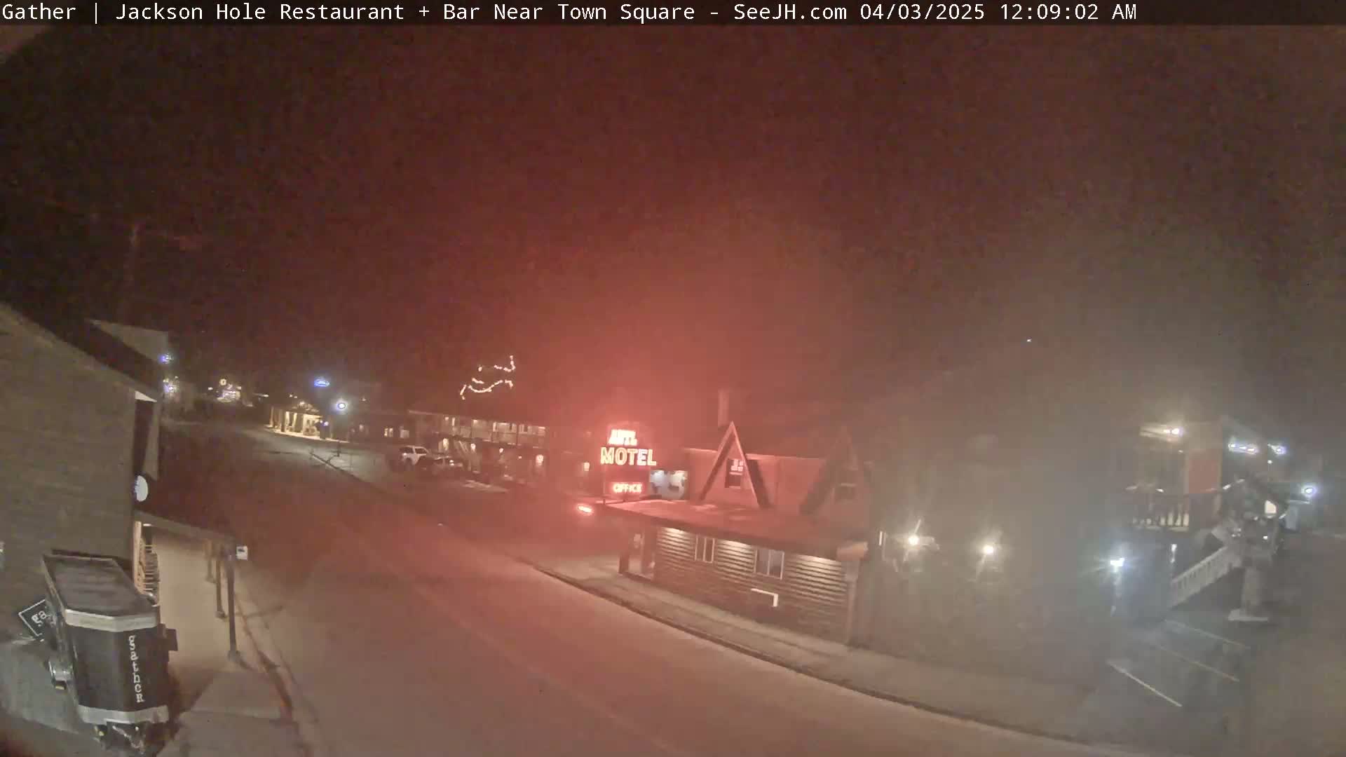 A nighttime, hazy view of a street scene shows a motel and other buildings with some vehicle lights visible.