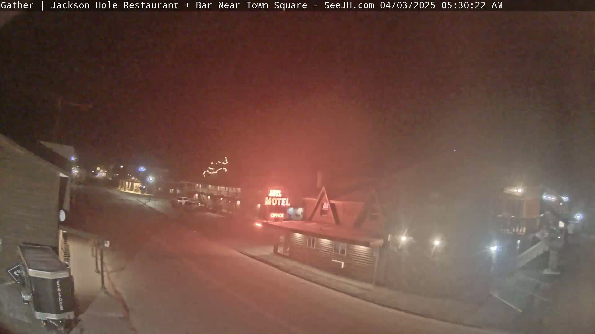 A nighttime, snowy street scene shows a motel and other buildings with faint lights visible in hazy conditions.