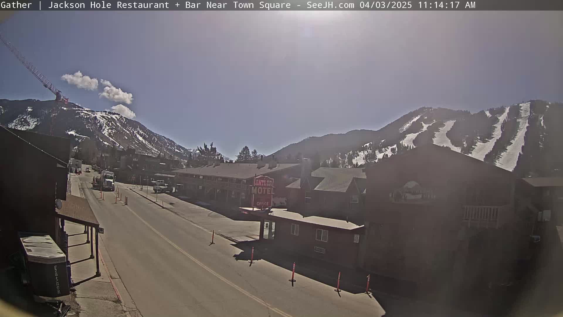 A sunny day reveals a street scene with a motel, mountains showing ski runs in the background, and a construction crane on a hillside.