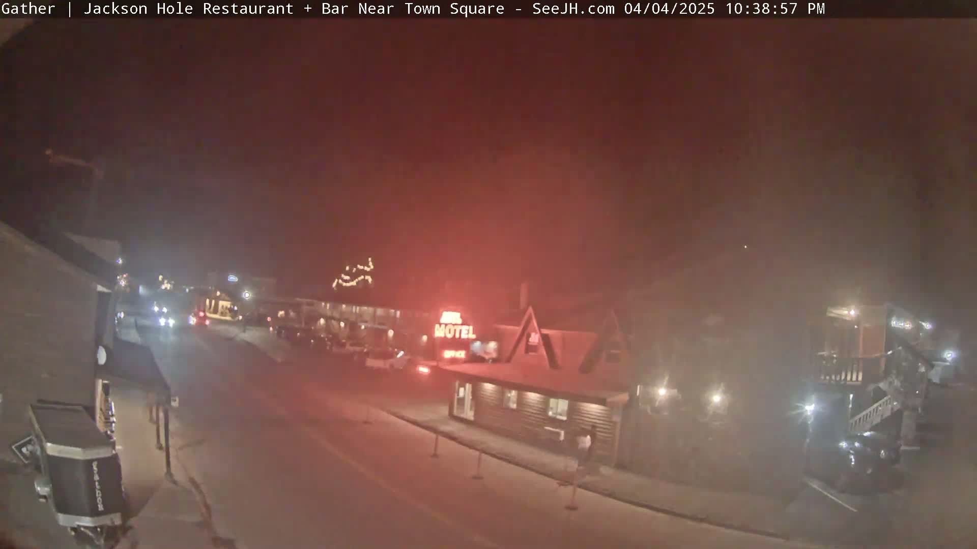 A nighttime, hazy street scene shows a motel and other buildings with some cars and pedestrians visible.