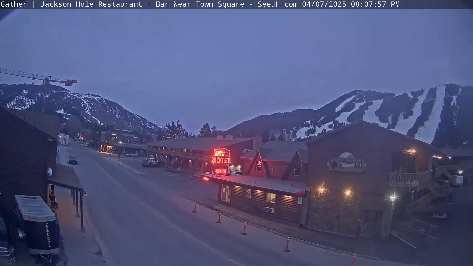 A twilight view of a town nestled in a mountain valley, with a motel illuminated and a ski slope visible on the mountainside.