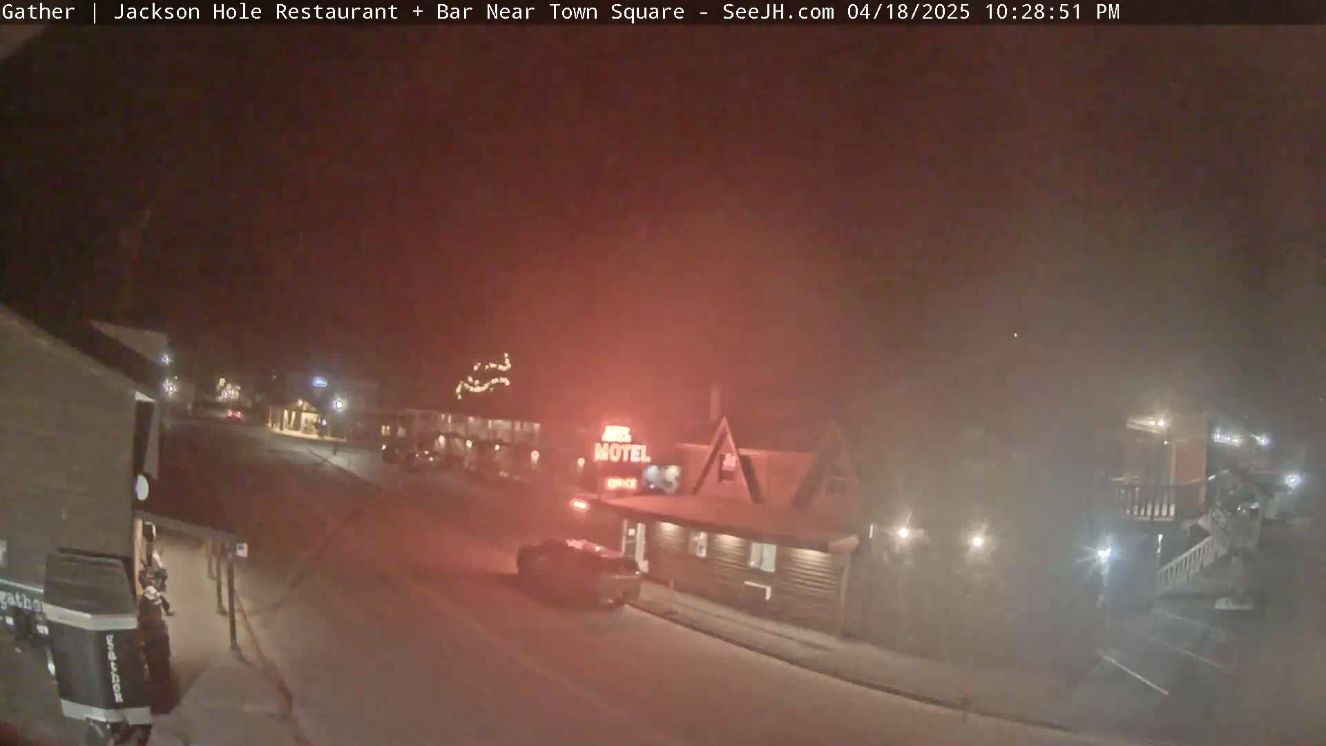 A nighttime street scene shows a motel and other buildings under hazy conditions, with a few vehicles visible.