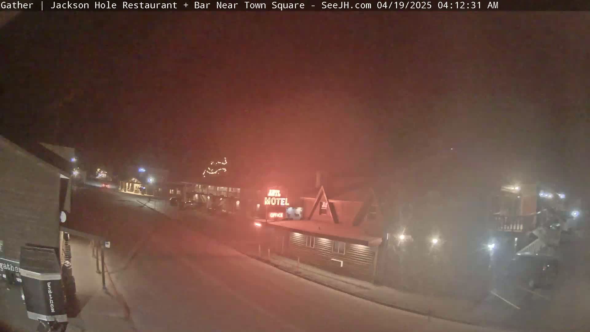 A dimly lit, snowy street at night shows buildings and a motel, with hazy conditions reducing visibility.