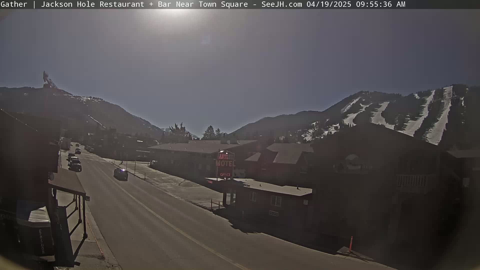 A sunny day reveals a town street scene nestled in a valley, with mountains showing visible ski slopes in the background.