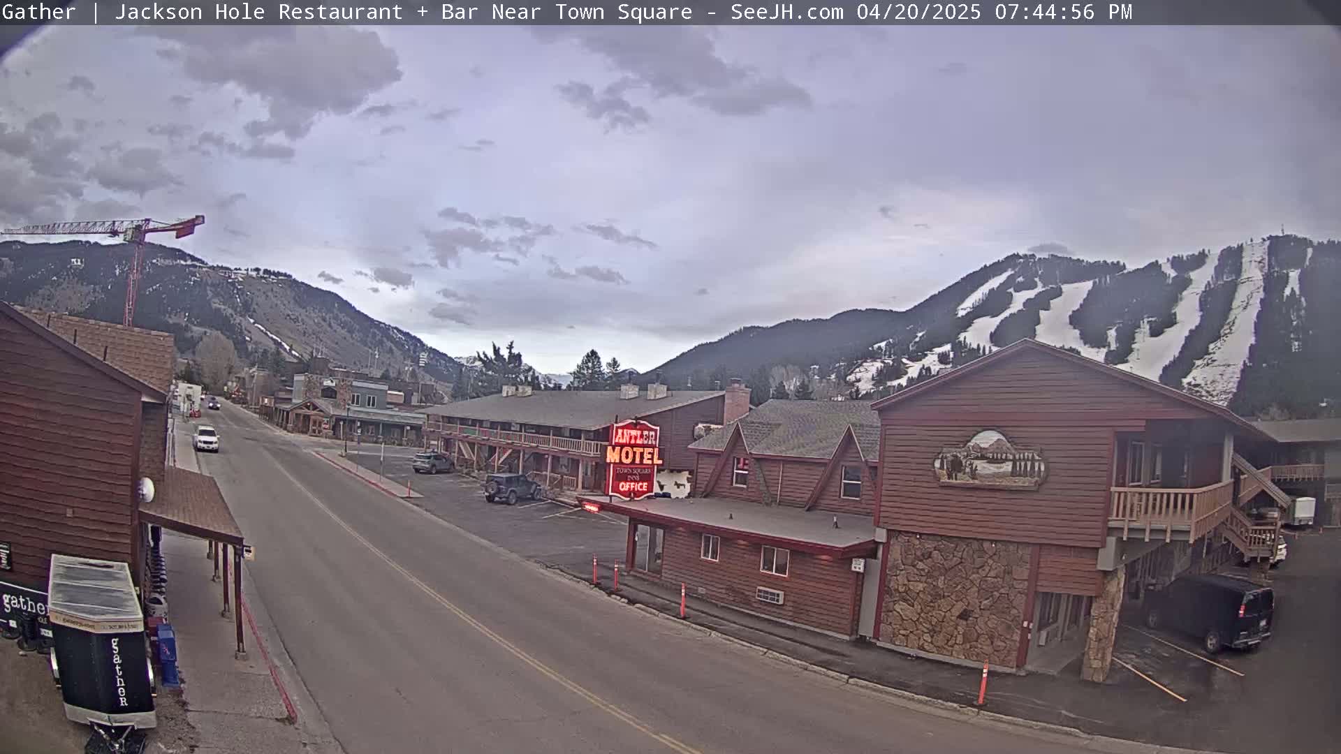 A street scene shows a partly cloudy sky over a town nestled in mountains with a ski slope visible in the background.