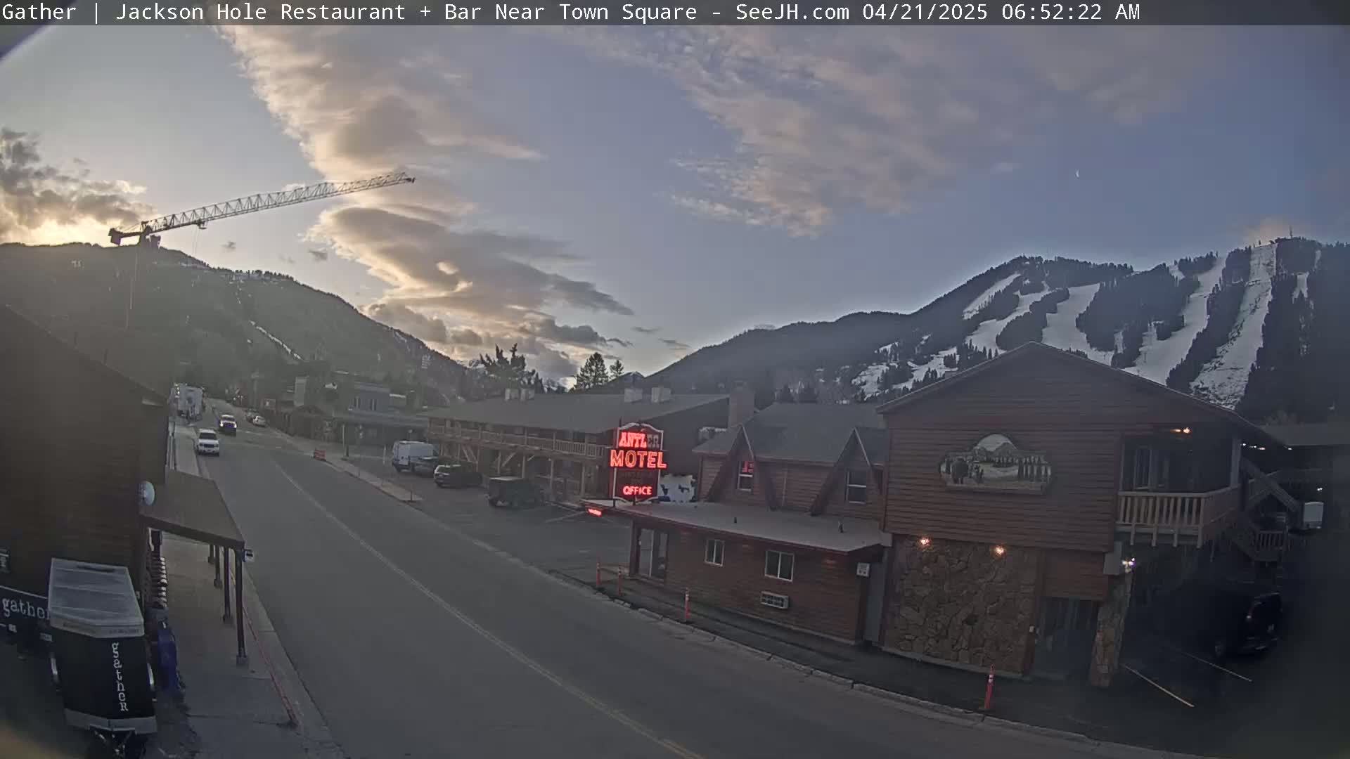A mostly clear twilight sky over a mountain with ski runs, shows a town street with cars and buildings, including a motel, and a construction crane.
