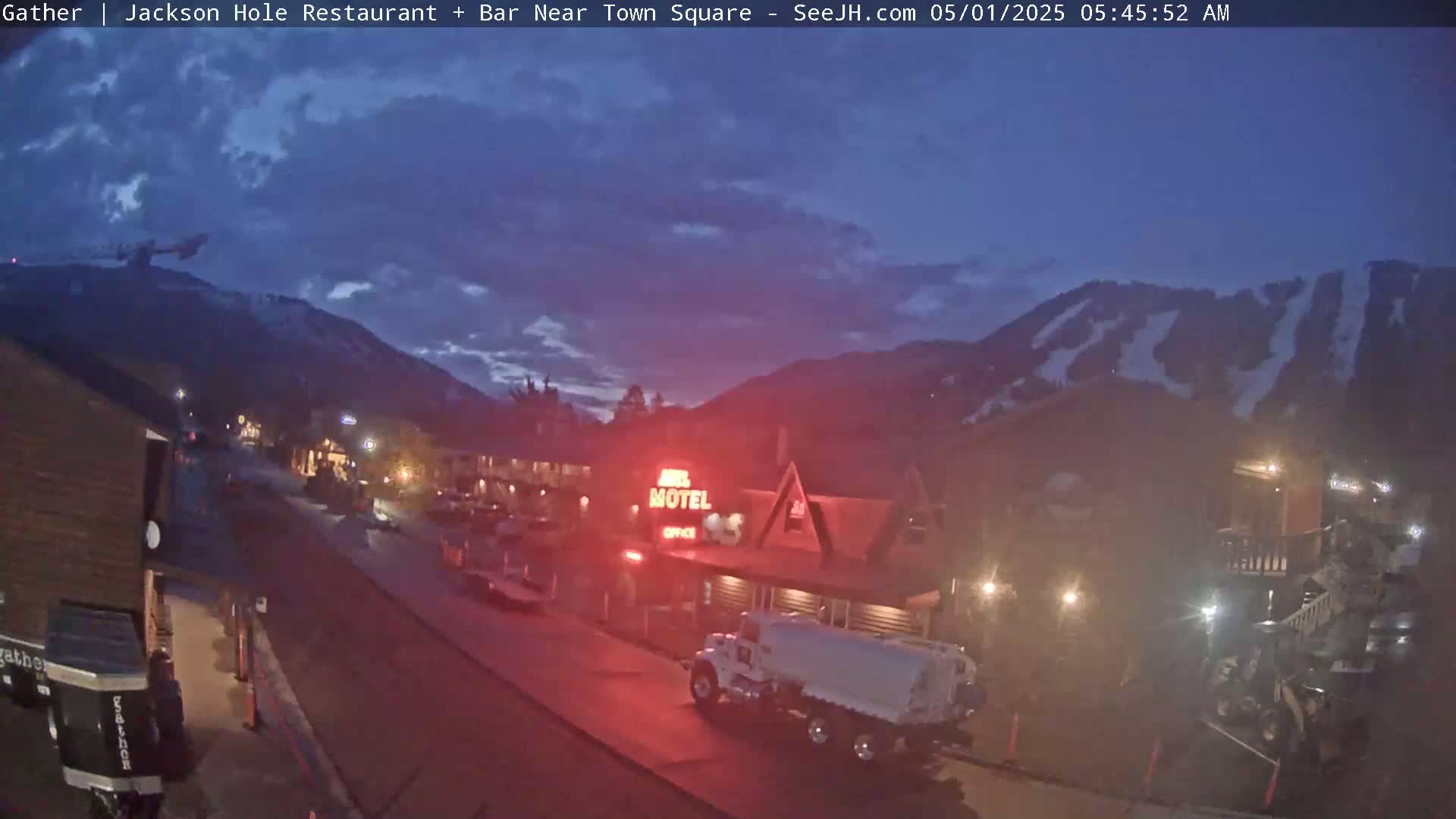 A twilight view of a town, possibly a ski resort, with a motel and a fuel truck, under a partly cloudy sky.