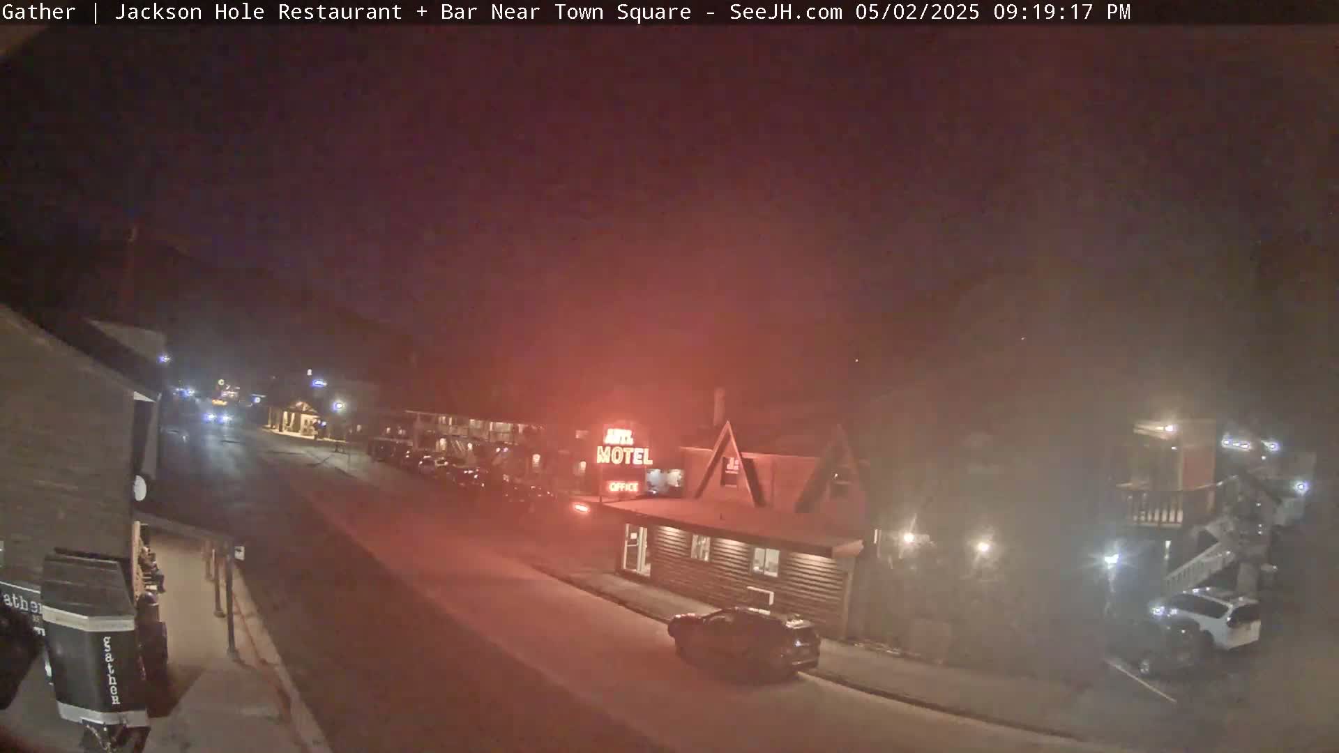 A nighttime street scene shows a motel and a few vehicles under hazy, dark conditions.