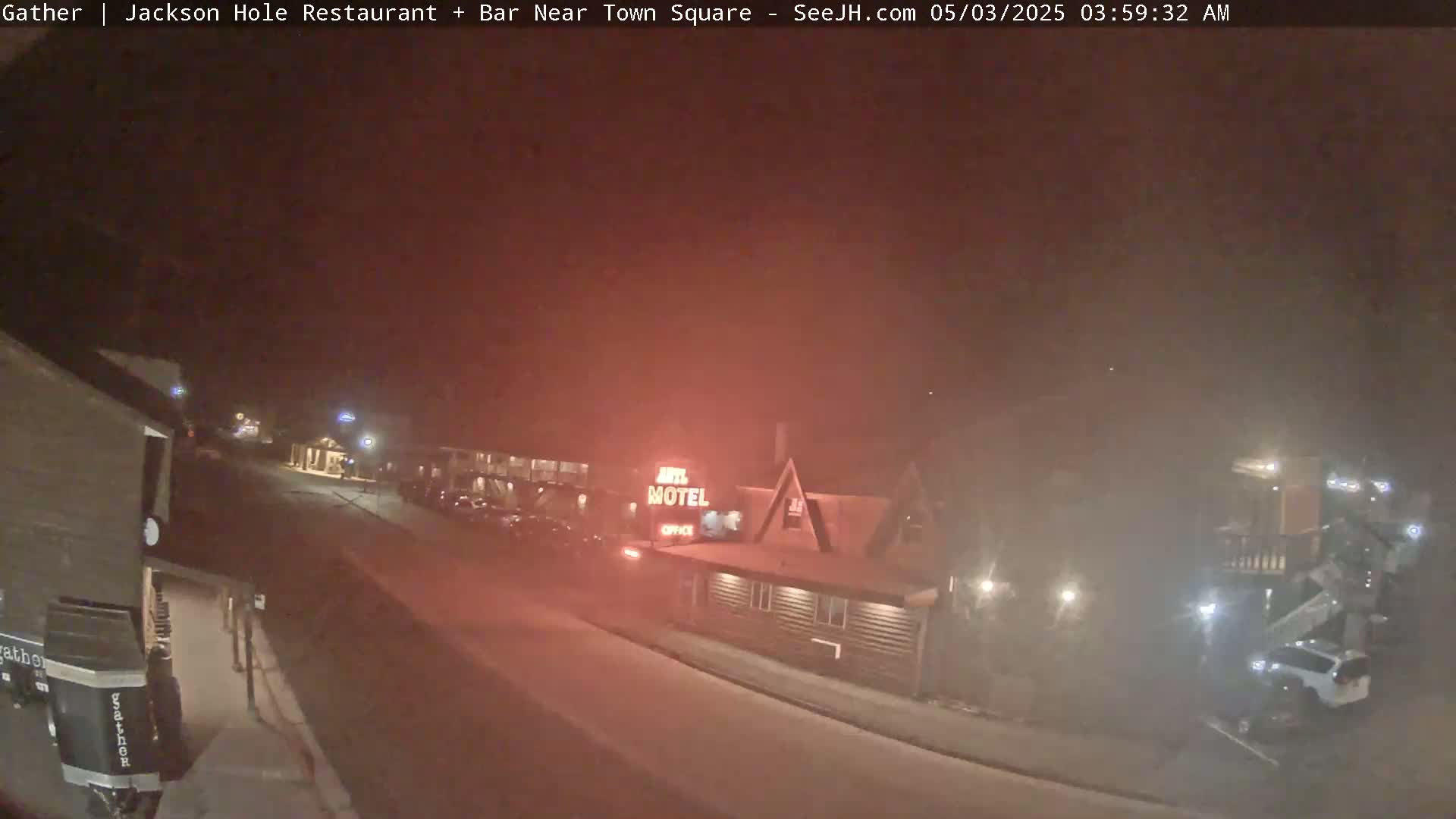 A nighttime street scene shows a motel and parked cars under hazy or foggy conditions.