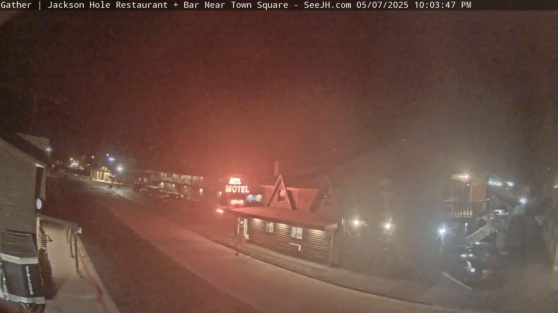 A nighttime, hazy view of a motel and street with a few cars and people visible.