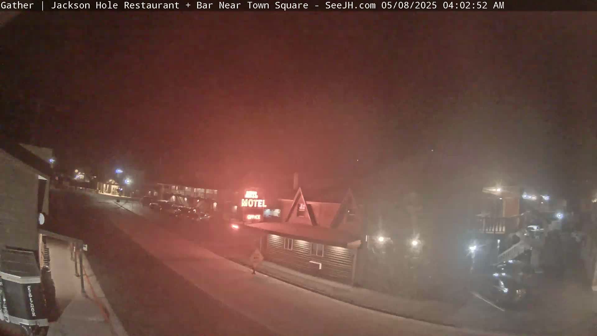 A nighttime street scene shows a motel and several parked cars under hazy conditions.