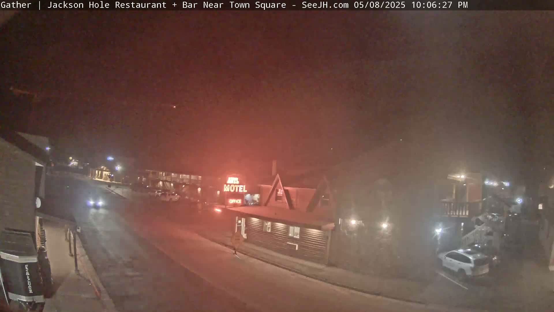 A nighttime street scene shows a motel and a few vehicles under hazy, dark conditions.