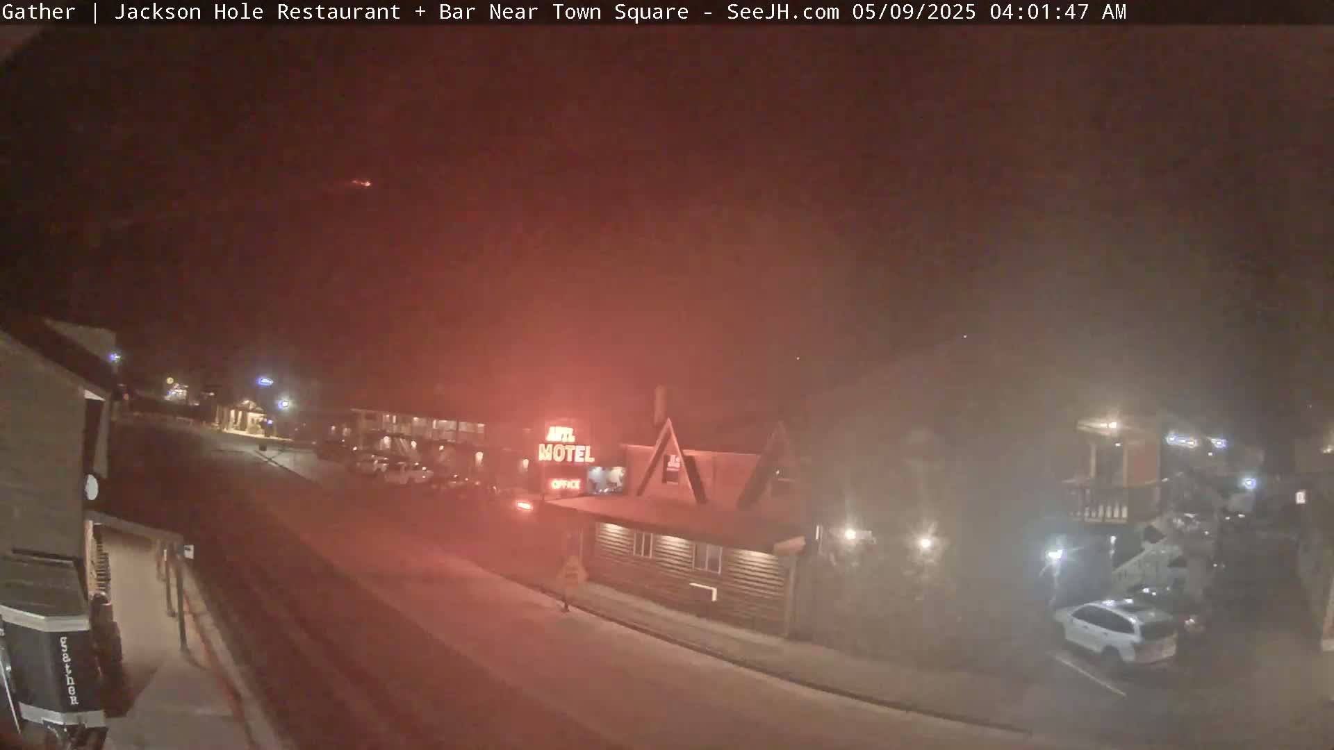 A nighttime street scene shows a motel and parked cars under hazy, reddish-lit conditions.