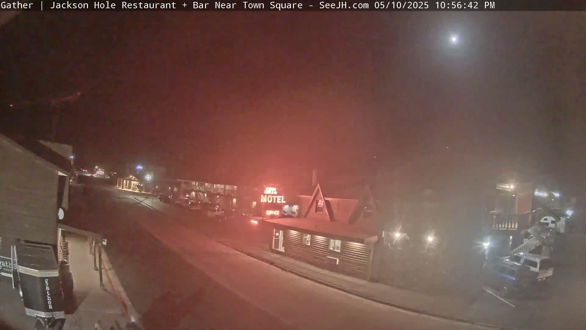 A hazy night scene shows a motel and a street with parked vehicles under a bright light in the sky.