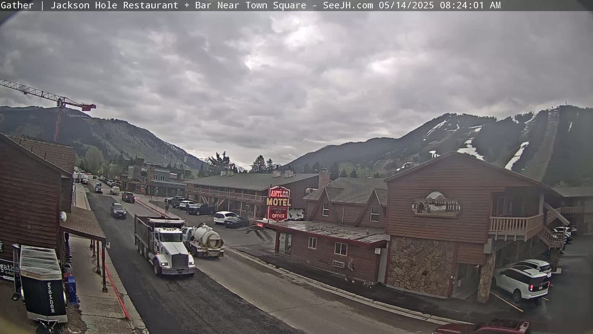 A street scene in a mountainous area shows overcast skies, a road with vehicles including a dump truck and a vacuum truck, and buildings including a motel.