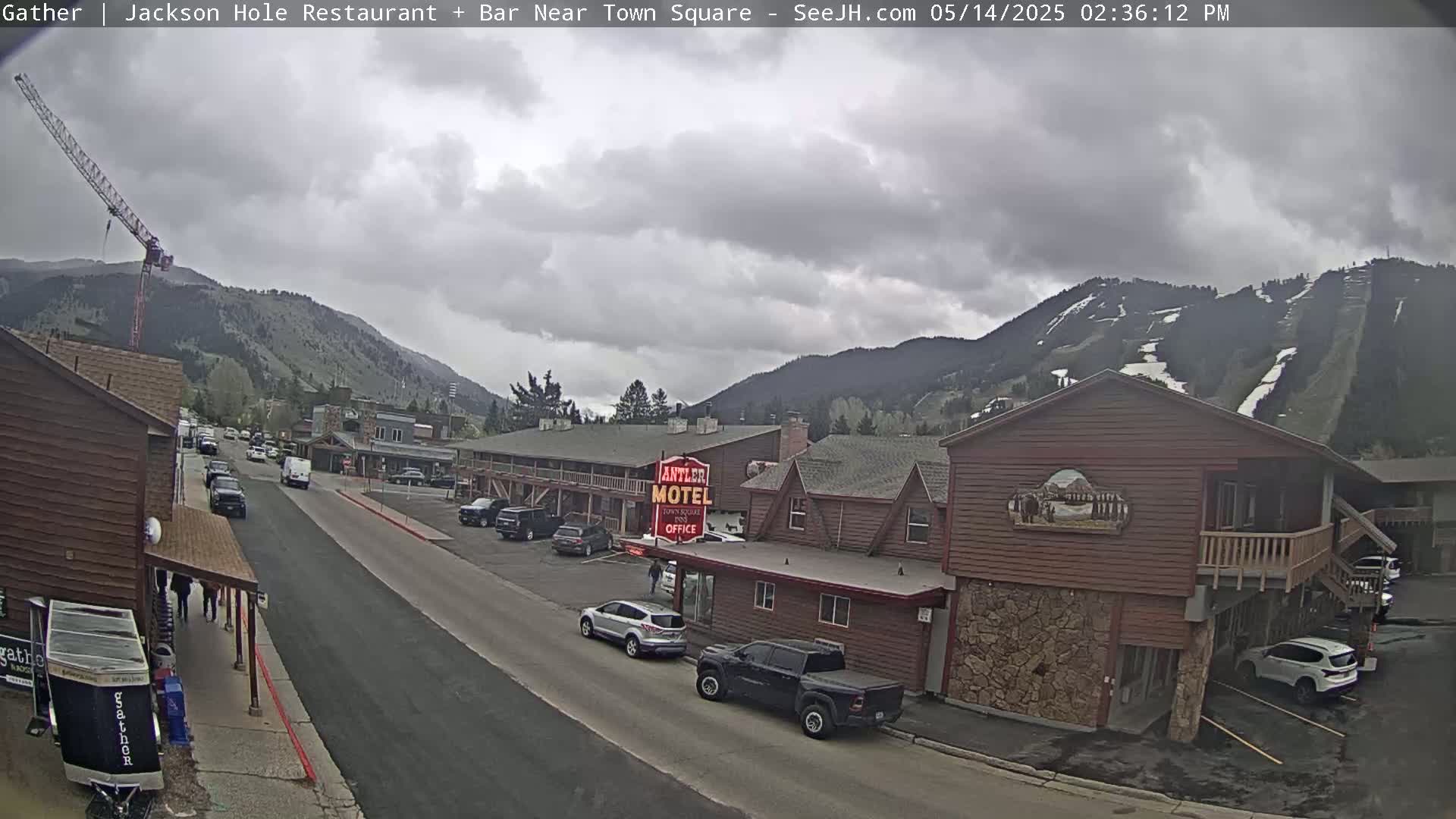 A street scene shows overcast skies over a town nestled in mountains with a motel, vehicles, and a construction crane visible.
