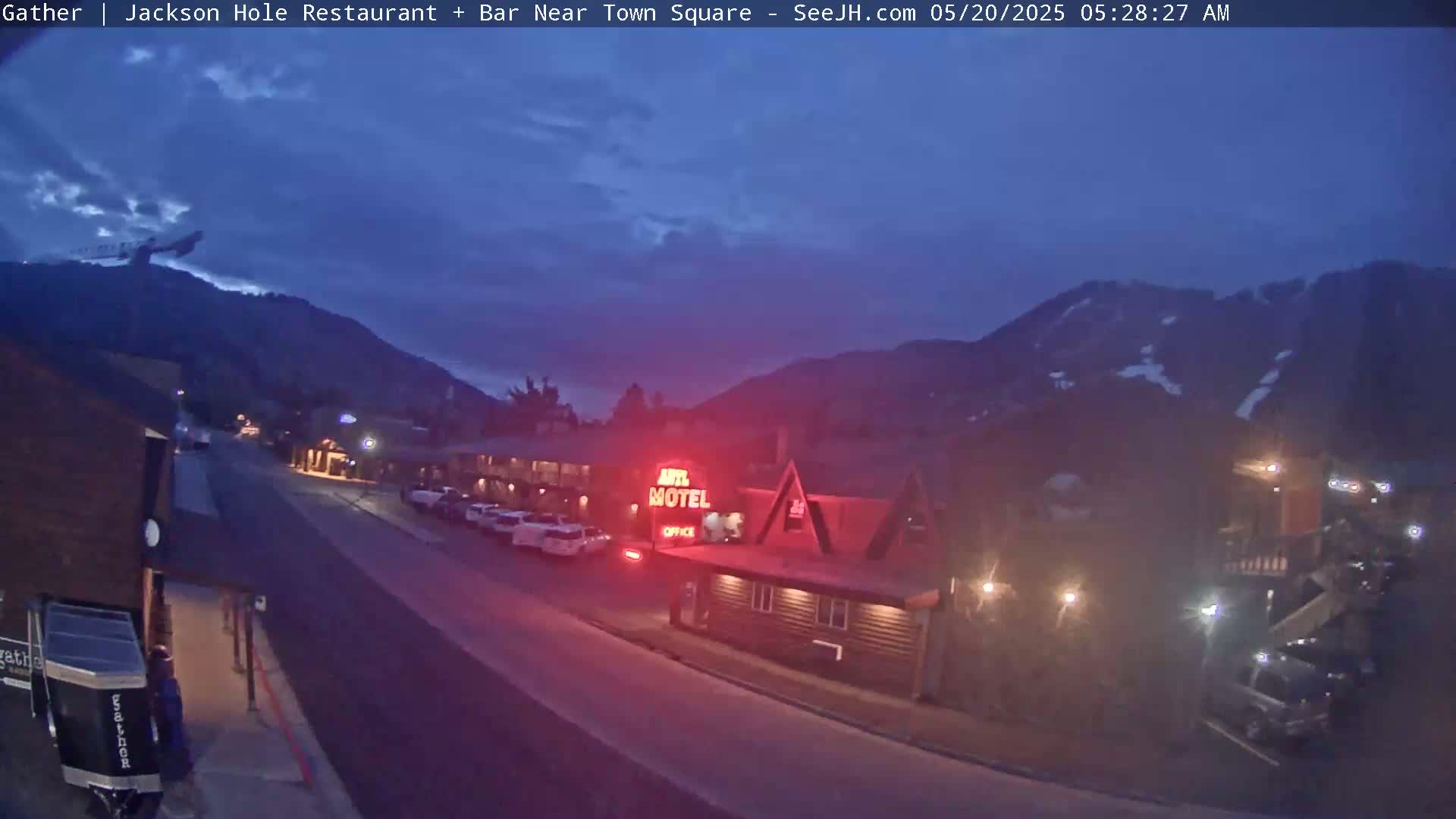 A street scene at twilight shows a motel and several parked cars, with mountains in the background under a mostly clear, dark blue sky.
