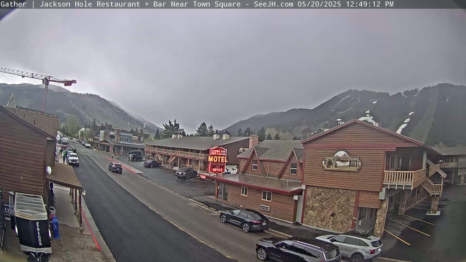 A street scene shows a motel and other buildings under an overcast sky, with mountains in the background and cars parked along the street.